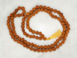 Original 5 Mukhi Rudraksha Mala 108+1 beads with golden tassel laid on marble surface