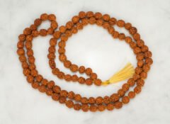 Original 5 Mukhi Rudraksha Mala 108+1 beads with golden tassel laid on marble surface