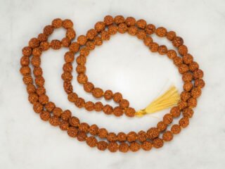 Original 5 Mukhi Rudraksha Mala 108+1 beads with golden tassel laid on marble surface