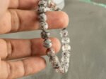 Hand holding grey jasper stone bracelet showing natural texture and size