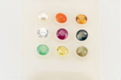 9 loose Navratna gemstones on white background - Ruby, Pearl, Emerald, Pukhraj, Neelam, Gomed, Lehsunia, Moonga, American Diamond