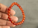 Hand holding translucent Red Quartz bracelet showing orange red beads and elasticity