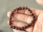 Hand holding 8mm Red Tiger's Eye gemstone bracelet showing stimulating color