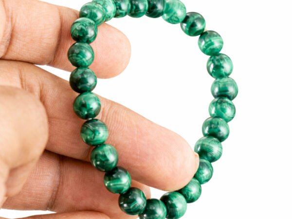 Hand holding a genuine green Malachite gemstone bracelet showing scale and bead details.