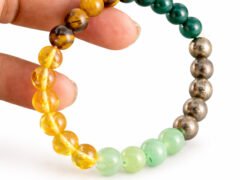 Hand holding a genuine multi-color Money Magnet gemstone bracelet showing scale and varying bead textures.