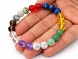 Hand holding a genuine multi-color Navratna gemstone bracelet showing scale and varying bead colors.