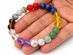 Hand holding a genuine multi-color Navratna gemstone bracelet showing scale and varying bead colors.