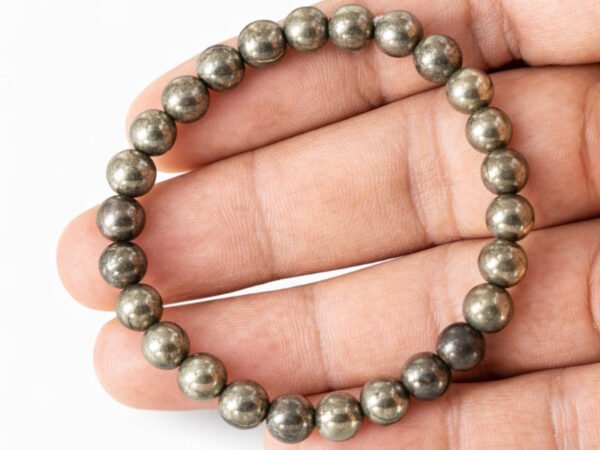 Hand holding a genuine golden Pyrite gemstone bracelet flat across the palm, showing scale and metallic bead details.