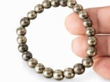 Fingers holding a genuine natural Pyrite gemstone bracelet vertically, showcasing the 8mm golden beads.