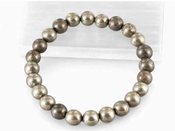 Close-up of an authentic metallic golden Pyrite stone bracelet resting on a white textured display plate.