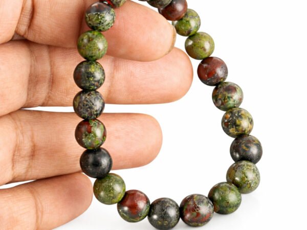 Fingers holding a genuine natural Red Bloodstone gemstone bracelet vertically, showcasing the 8mm beads and their earthy red and green textures.