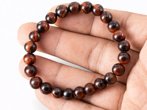 Hand holding a genuine natural Red Tiger Eye gemstone bracelet flat across the palm, showing scale and bead details.
