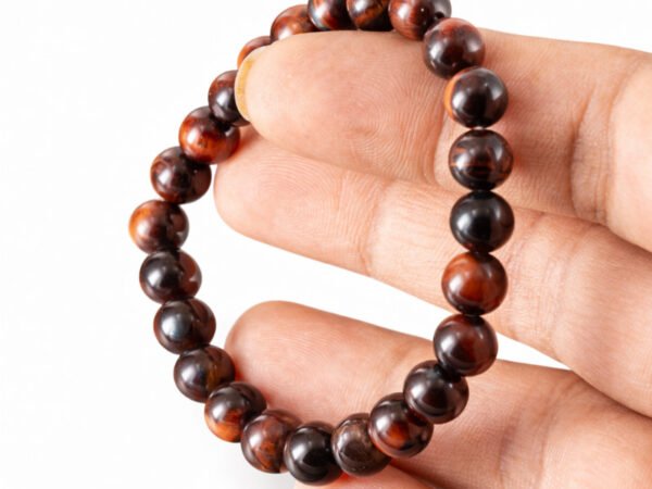 Fingers holding a genuine natural Red Tiger Eye gemstone bracelet vertically, showcasing the 8mm beads.