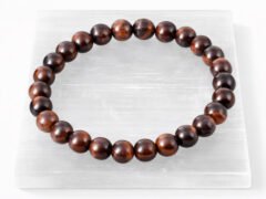 Authentic natural Red Tiger Eye gemstone bracelet resting flat on a white textured display plate.