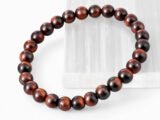 Close-up of an authentic natural Red Tiger Eye stone bracelet resting on a white rectangular display plate.