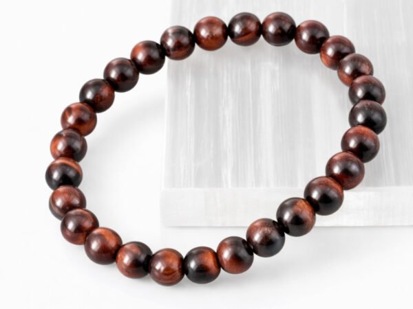 Close-up of an authentic natural Red Tiger Eye stone bracelet resting on a white rectangular display plate.