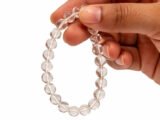 Fingers holding a genuine natural Rock Crystal Sphatik gemstone bracelet vertically, showcasing the clear 8mm beads.