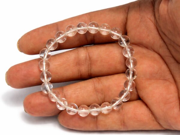 Hand holding a genuine natural Rock Crystal Sphatik gemstone bracelet flat across the palm, showing scale and clarity details.