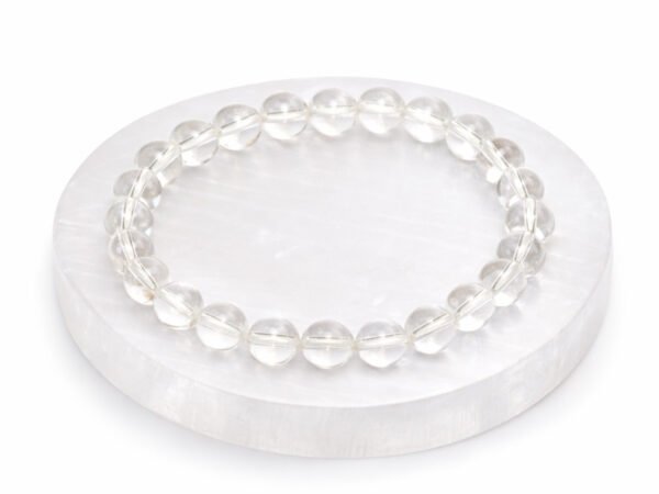 Authentic natural Rock Crystal Sphatik gemstone bracelet resting flat on a round white display plate.