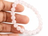 Hand holding a genuine natural Rose Quartz gemstone bracelet, showing scale and soft pink bead details.