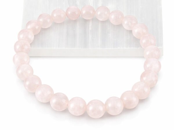Close-up of an authentic natural Rose Quartz stone bracelet resting partially on a white rectangular display plate.