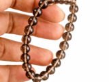 Fingers holding a genuine natural Smoky Quartz gemstone bracelet, showcasing the 8mm beads and their translucent brown color.