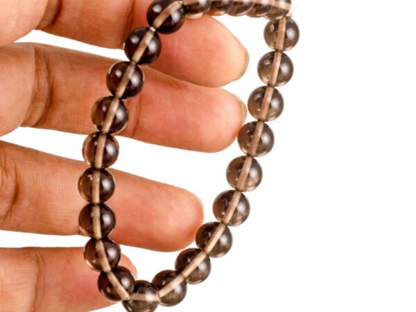 Fingers holding a genuine natural Smoky Quartz gemstone bracelet, showcasing the 8mm beads and their translucent brown color.