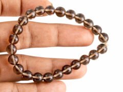 Hand holding and gently stretching a genuine natural Smoky Quartz gemstone bracelet, showing the elastic cord and 8mm brown beads.