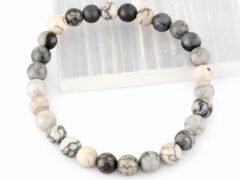 Authentic natural Spider Web Agate gemstone bracelet resting flat on a white square display plate.
