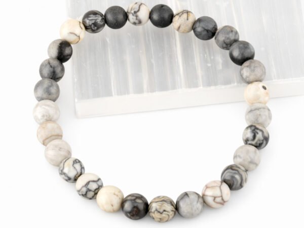 Authentic natural Spider Web Agate gemstone bracelet resting flat on a white square display plate.