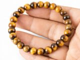 Hand holding a genuine natural Tiger Eye gemstone bracelet flat across the palm, showcasing the golden-yellow banded 8mm beads.