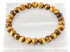 Authentic natural Tiger Eye gemstone bracelet resting flat on a white square display plate.