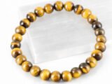 Close-up of an authentic natural Tiger Eye stone bracelet resting on a white rectangular display plate.