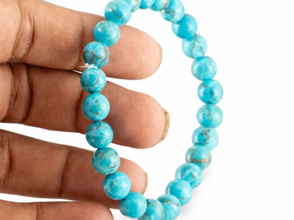 Fingers gently holding a genuine Turquoise Firoza gemstone bracelet vertically, showcasing the striking 8mm sky blue beads.