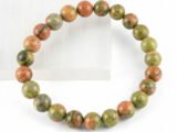 Authentic natural Unakite gemstone bracelet resting on the edge of a white textured display plate.