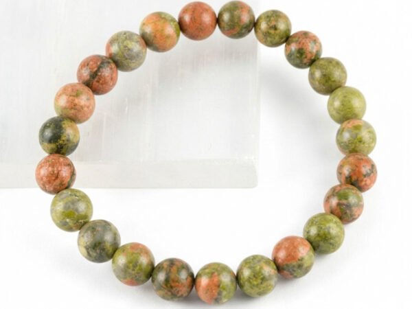 Authentic natural Unakite gemstone bracelet resting on the edge of a white textured display plate.
