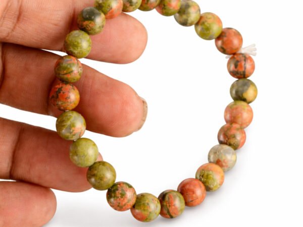 Hand holding a genuine natural Unakite gemstone bracelet vertically, showcasing the mottled green and pink 8mm beads.