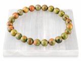 Authentic natural Unakite gemstone bracelet resting flat on a white square textured display plate.